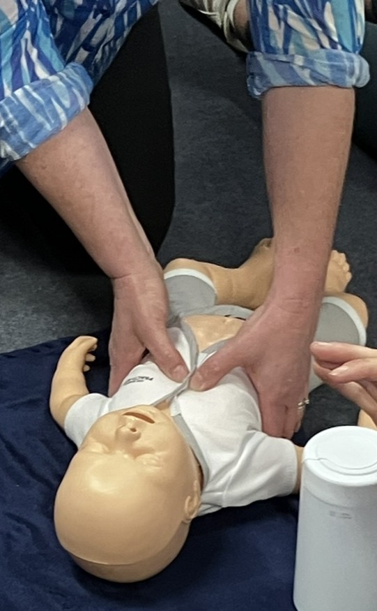 Someone performing chest compressions for CPR on an infant manikin.